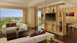 Una sala de estar moderna con sofá, mesa de centro y televisor, que ofrece vistas a la ciudad a través de amplios ventanales.