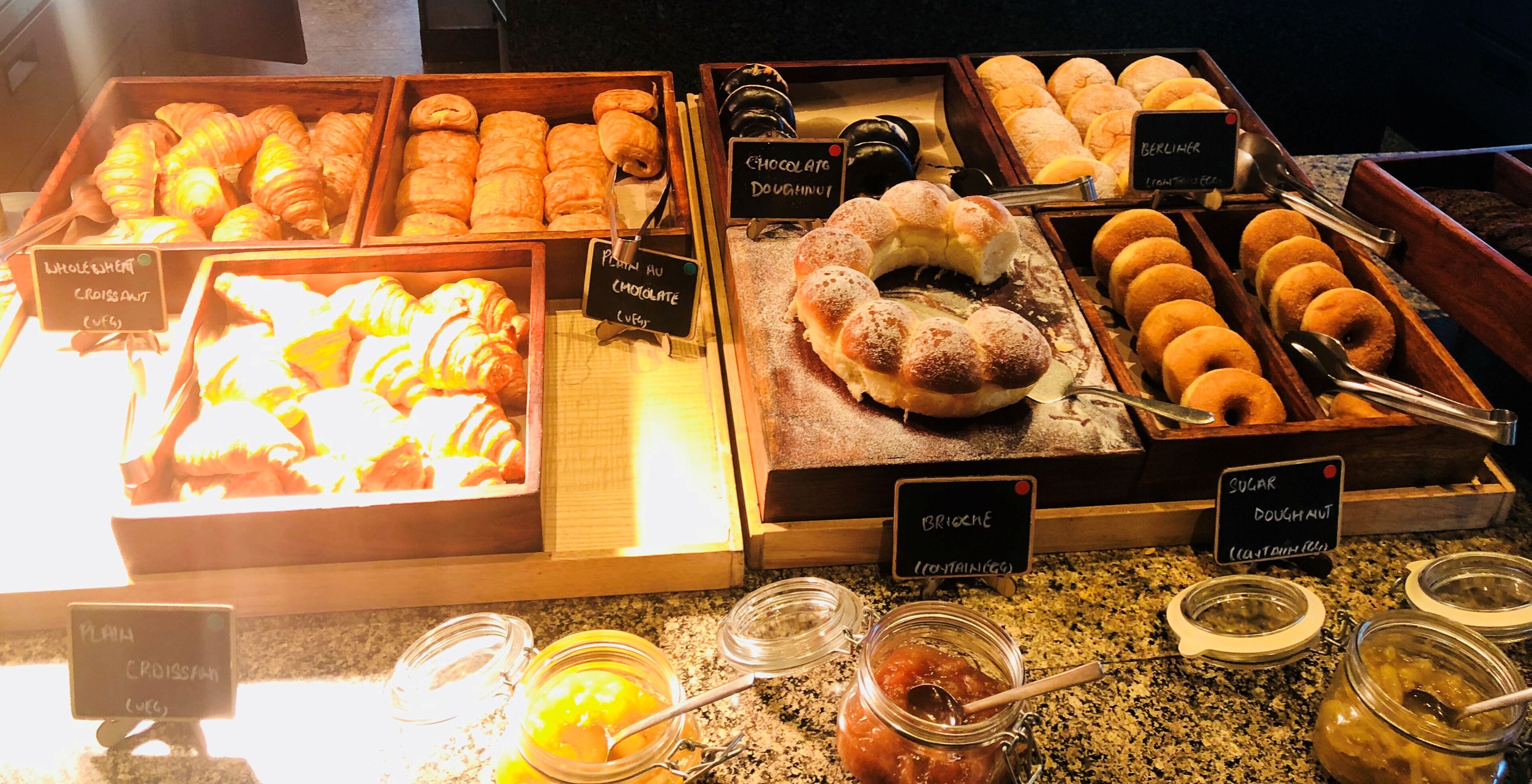 A bakery display with various baked goods like croissants, chocolate doughnuts, and bread rolls.