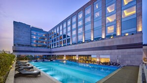 Un hotel moderno con una amplia piscina exterior, varios niveles y una fachada bien iluminada.