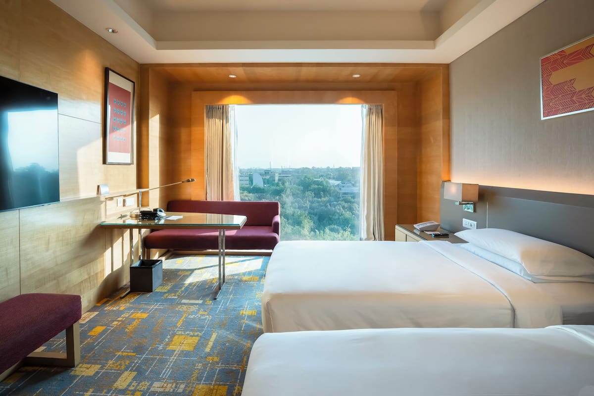A hotel room with a bed, a desk, a chair, and a large window with a city view.