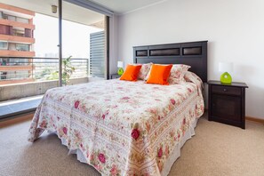 A bedroom with a large bed, two nightstands, a window with a view of buildings, and a balcony. - Livinnest Apartments (Santiago)