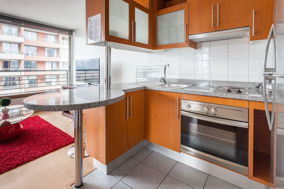 Una cocina moderna con armarios de madera, encimera de granito, electrodomésticos de acero inoxidable y una alfombra roja.