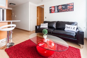 Un salon moderne avec une table basse en verre, un tapis rouge et un canapé en cuir noir agrémenté de coussins décoratifs.