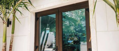 Una puerta de vidrio de entrada a un edificio con un letrero que dice 'Kids Club' y 'Zemi Beach'.