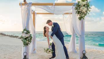 Ceremonia de boda en la playa con un arco de madera y cortinas blancas.