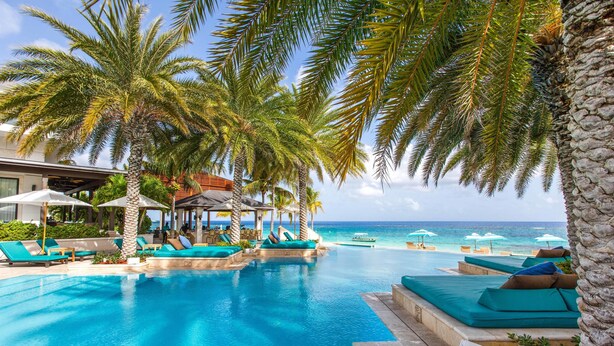 A pool area with lounge chairs and umbrellas, surrounded by palm trees and a view of the ocean. - Zemi Beach House, LXR Hotels & Resorts (Shoal Bay)
