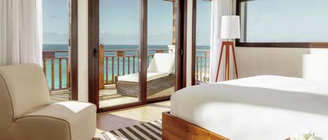 A hotel room with a large bed, a sofa, a lamp, and a view of the ocean through a sliding door.