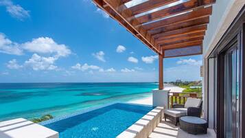Zona junto a la piscina con vistas al océano, una pérgola y mobiliario de exterior.