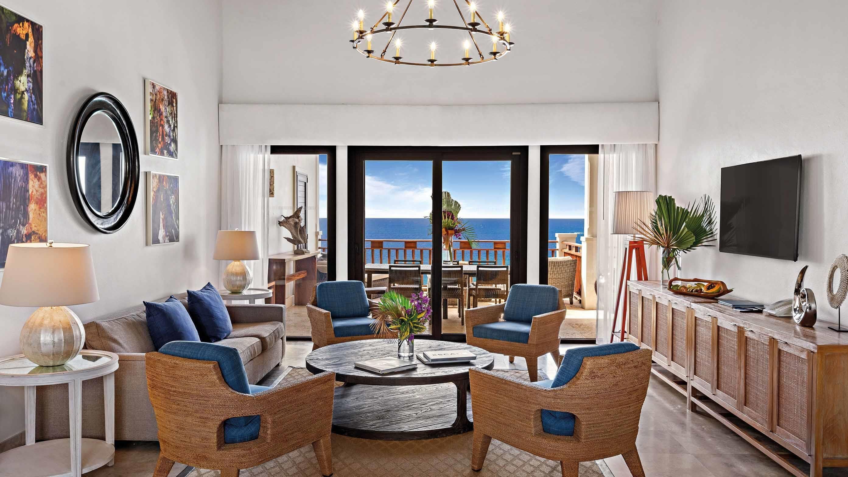 A spacious living room with a view of the ocean, featuring wicker furniture, a round coffee table, and a chandelier.