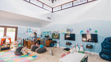 Amplia habitación con techo alto, ventanas grandes y una zona de juegos colorida con pufs y bolos.