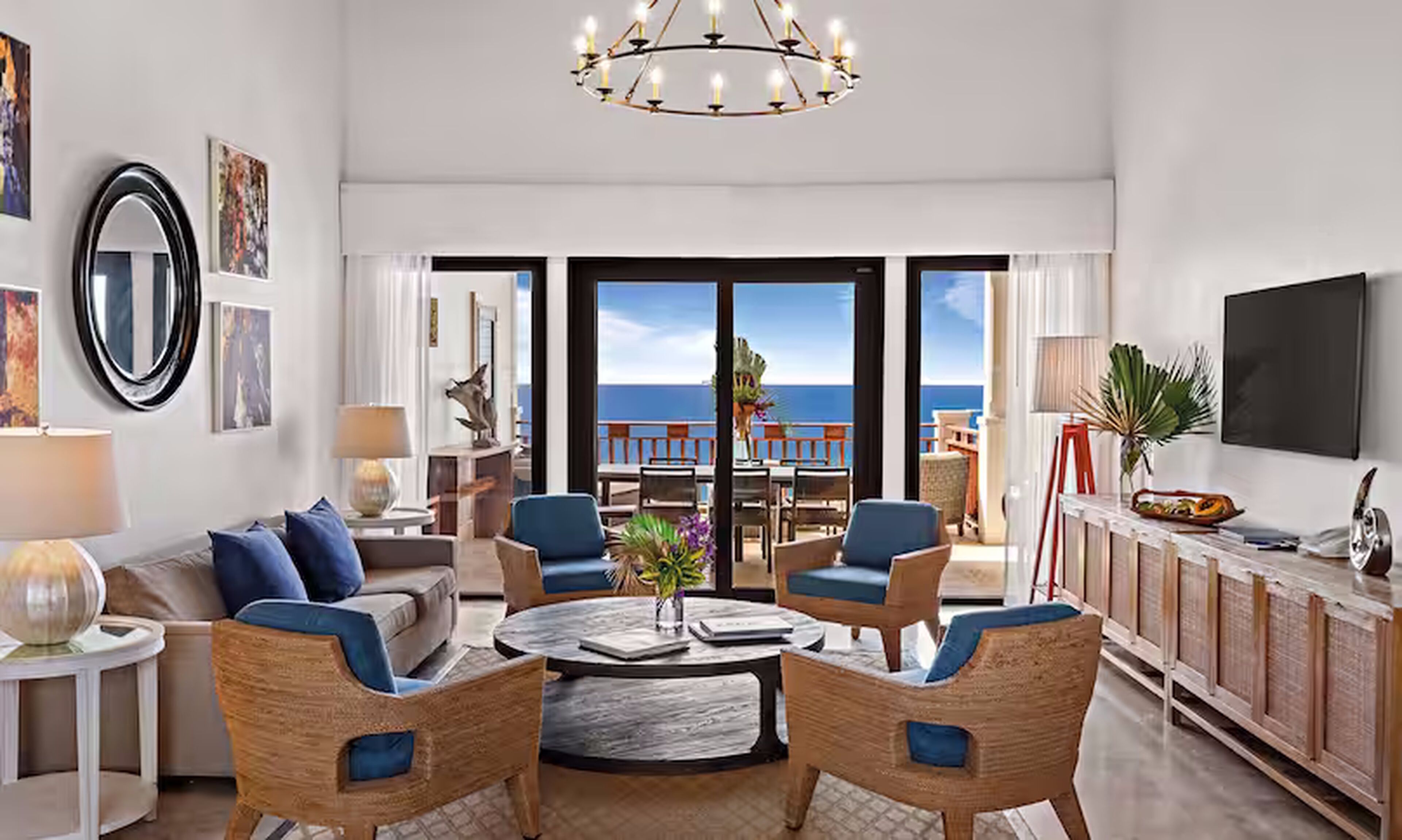 A modern living room with a view of the sea, featuring a sofa, chairs, a coffee table, and a TV.