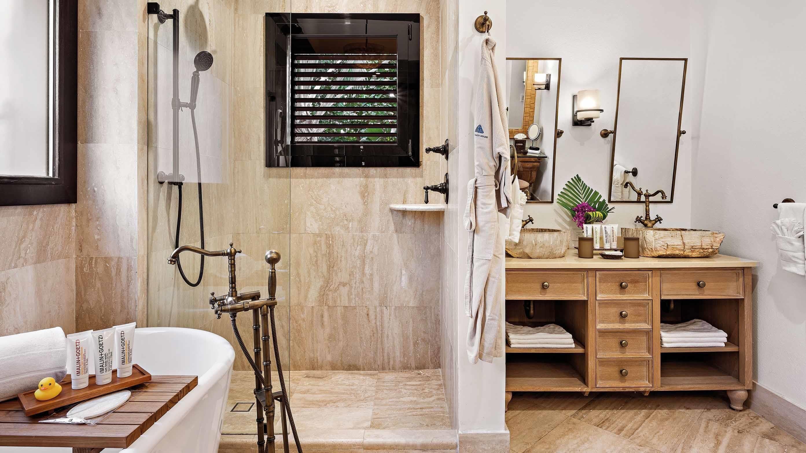 A bathroom with a bathtub, a wooden vanity with drawers, a large mirror, and a window with blinds.