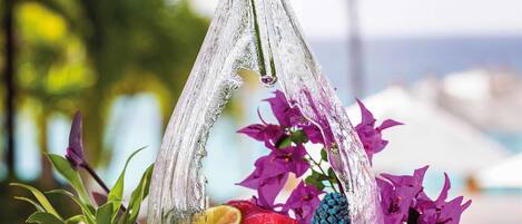 A sushi platter with shrimp and other seafood, garnished with purple flowers and a glass vase, set on a round, dark-colored tray.