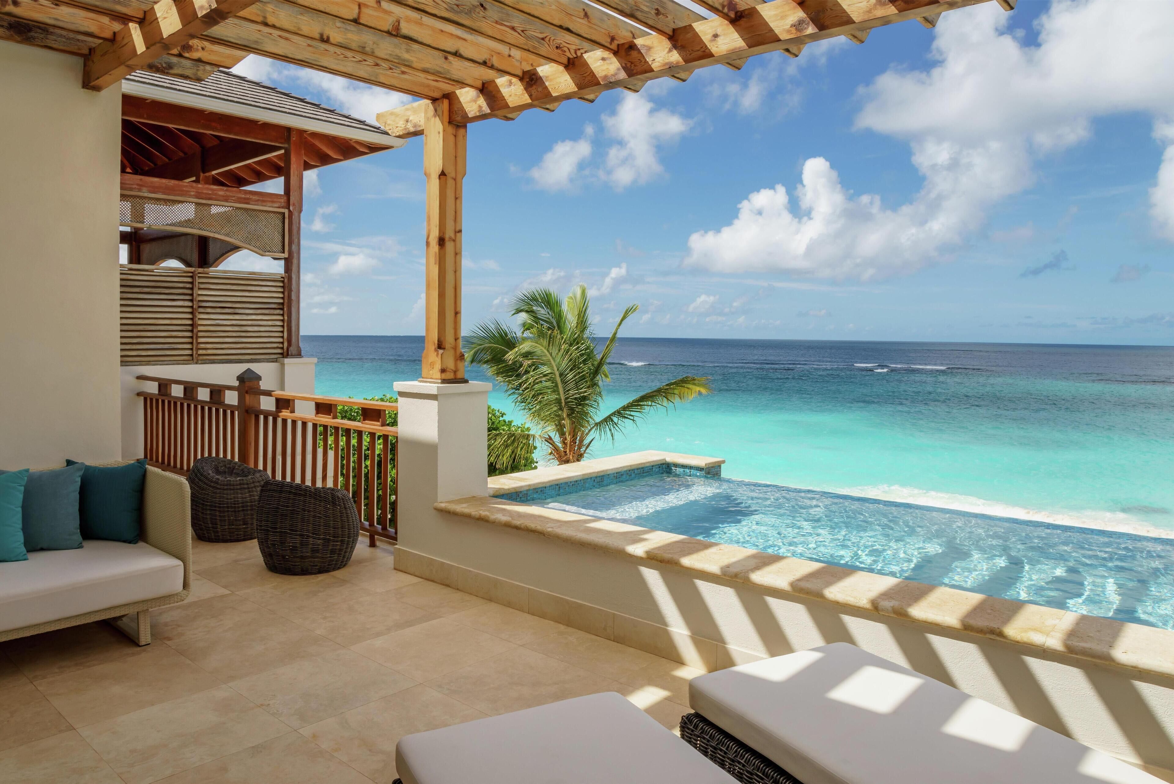 A balcony with a view of the ocean, a pool, and outdoor seating.