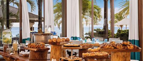 Un buffet proposant une variété de produits de boulangerie et une station de boissons, le tout avec une vue panoramique sur l’océan.