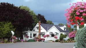 A white two-story house with a chimney, a porch with flower boxes, and a driveway. - Trenton Park Motel (Quinte West)