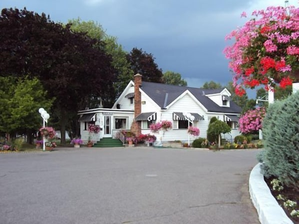 A white two-story house with a chimney, a porch with flower boxes, and a driveway.
