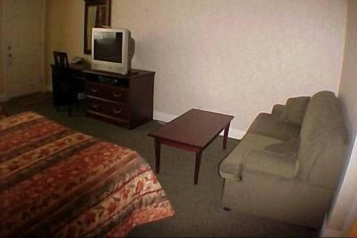 Quarto de hotel com uma cama, uma pequena escrivaninha com televisão, um sofá e uma poltrona.