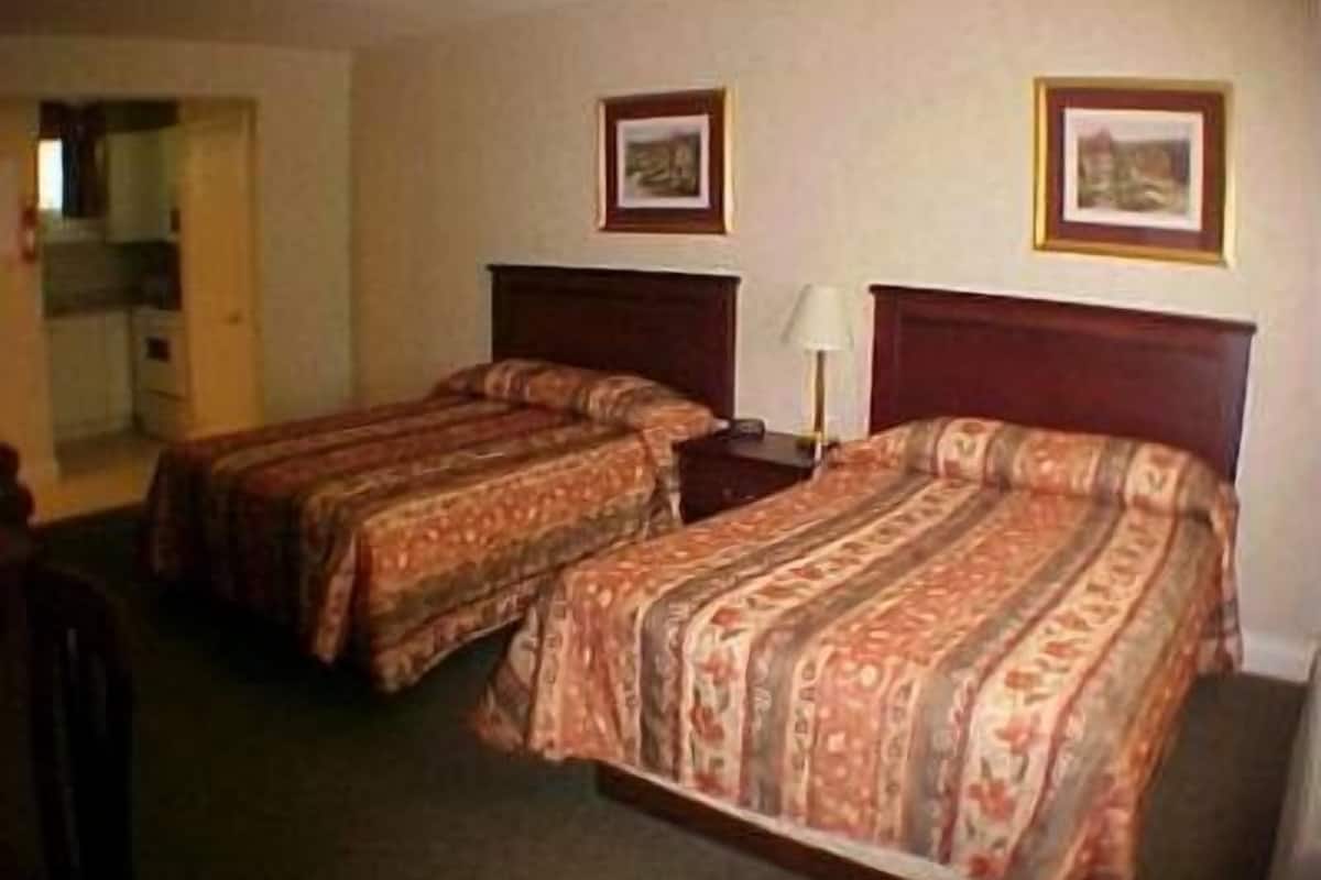 Quarto de hotel com duas camas de solteiro, uma escrivaninha e uma cadeira. Há quadros nas paredes.