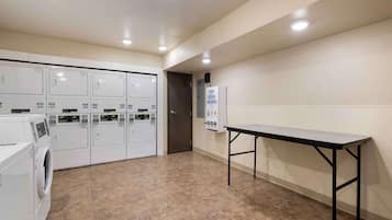 A laundry room with multiple washing machines, a table, and a soap dispenser on the wall.