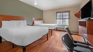 Ein Hotelzimmer mit zwei Betten, einem Fernseher, einem Schreibtisch und einem Fenster mit Jalousien.