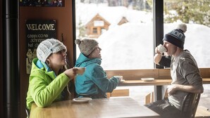 Una cafetería con interior de madera, un letrero de bienvenida y vistas a un paisaje nevado a través del ventanal.