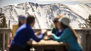 Un grupo de personas sentadas en una mesa con una montaña nevada al fondo.