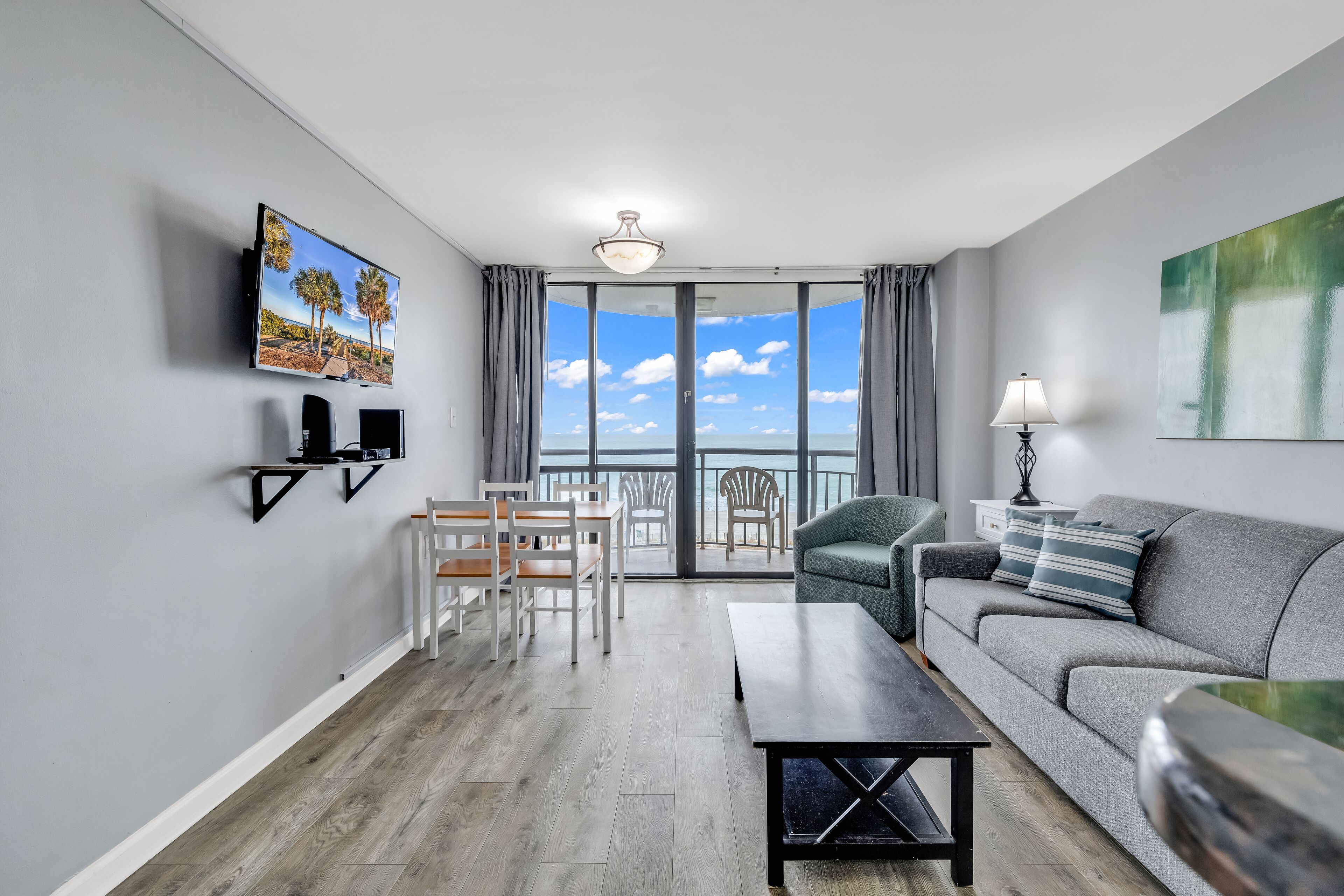 Un salon moderne avec balcon, un téléviseur à écran plat, un canapé, une table basse et un coin repas avec des chaises.