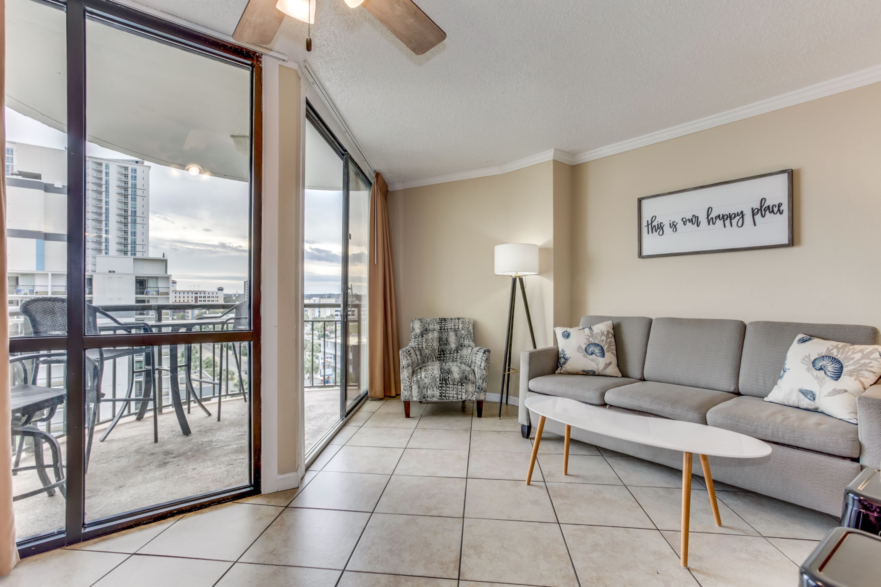Un salon moderne avec un canapé, un fauteuil à motifs, une lampe sur pied et une vue sur la ville grâce à de grandes fenêtres.