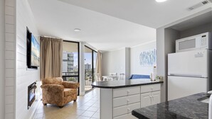 Eine moderne Küche mit weißen Schränken, einer schwarzen Arbeitsplatte und einer eingebauten Mikrowelle. Es gibt eine Essecke mit Tisch und Stühlen, und ein großes Fenster mit Blick auf die Stadt.