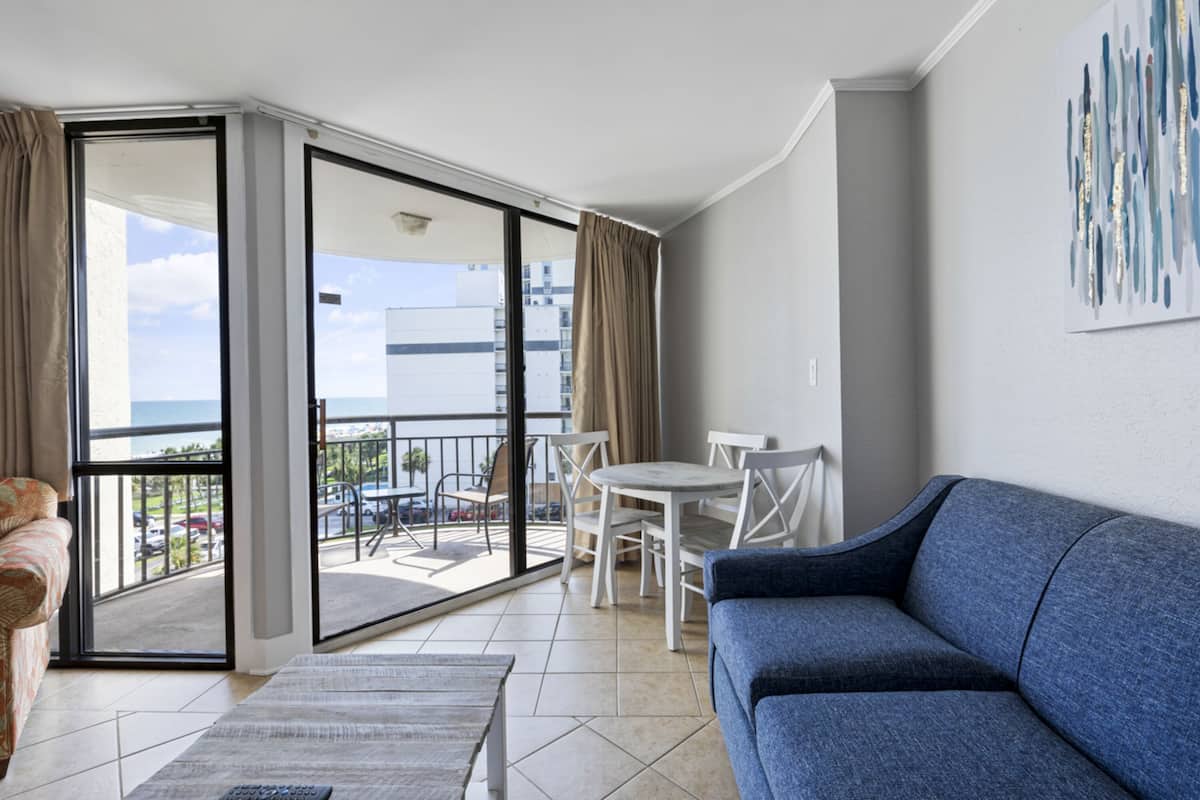 Un moderno salón con un sofá azul, una mesita y un balcón con vistas a la ciudad.