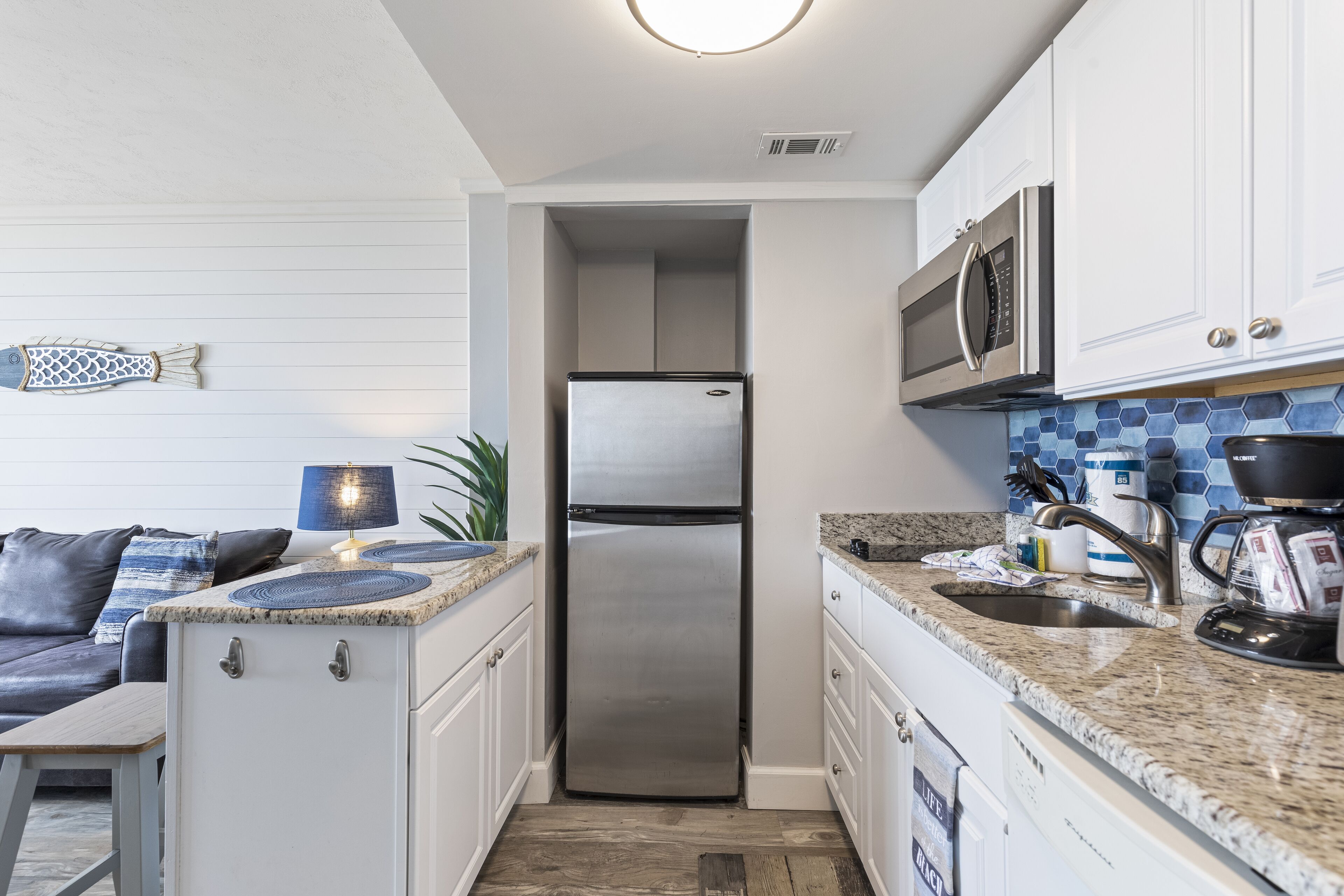A compact kitchen with white cabinets, a stainless steel refrigerator, a microwave, and a sink.
