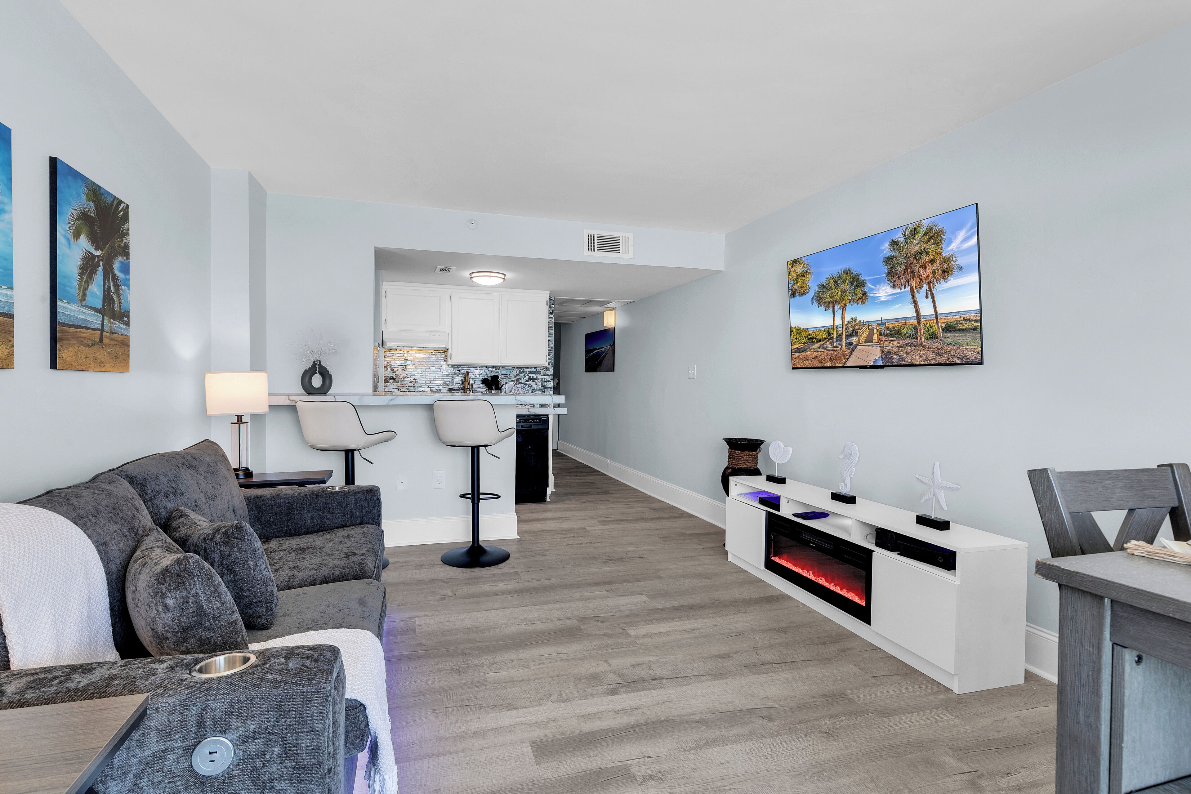 A modern living room with a grey sofa, a dining table, and a kitchen area in the background.