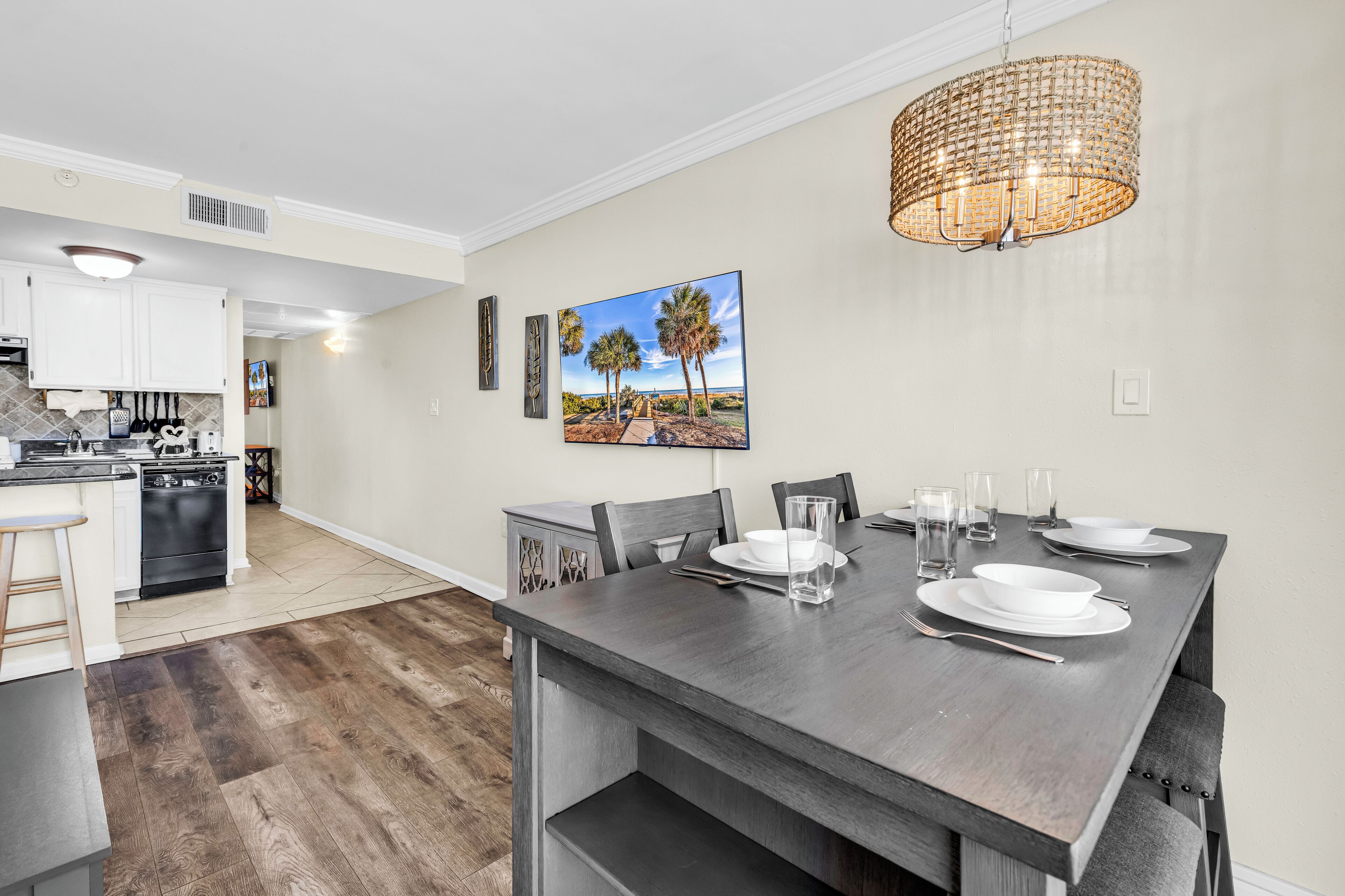 A modern kitchen with white cabinets, a dining area with a dark wooden table, and a hanging light fixture.