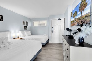Een hotelkamer met twee bedden, een witte deur, een schilderij van palmbomen en een witte badjas op het bed.
