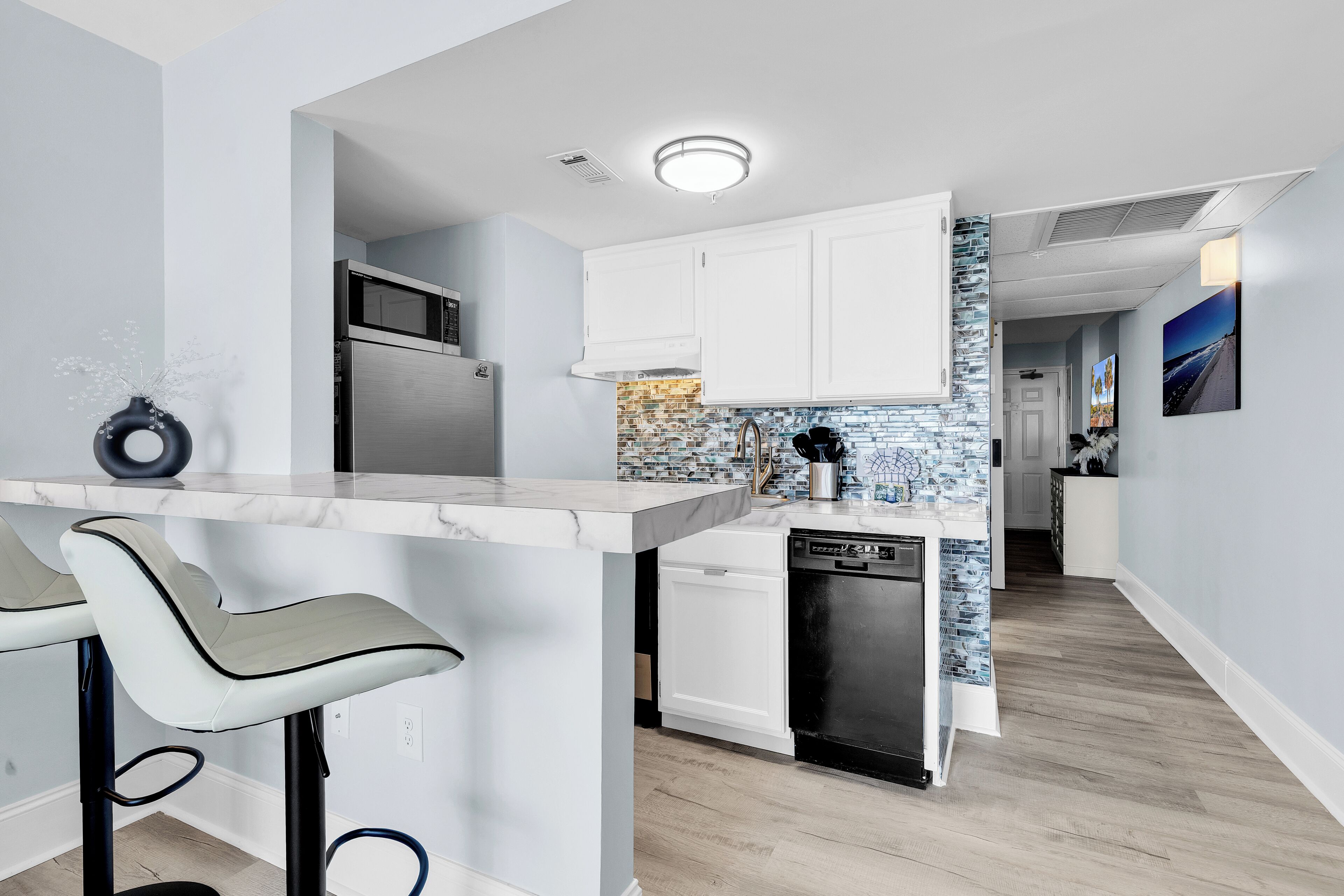 A modern kitchen with white cabinets, a marble countertop, and a dishwasher.