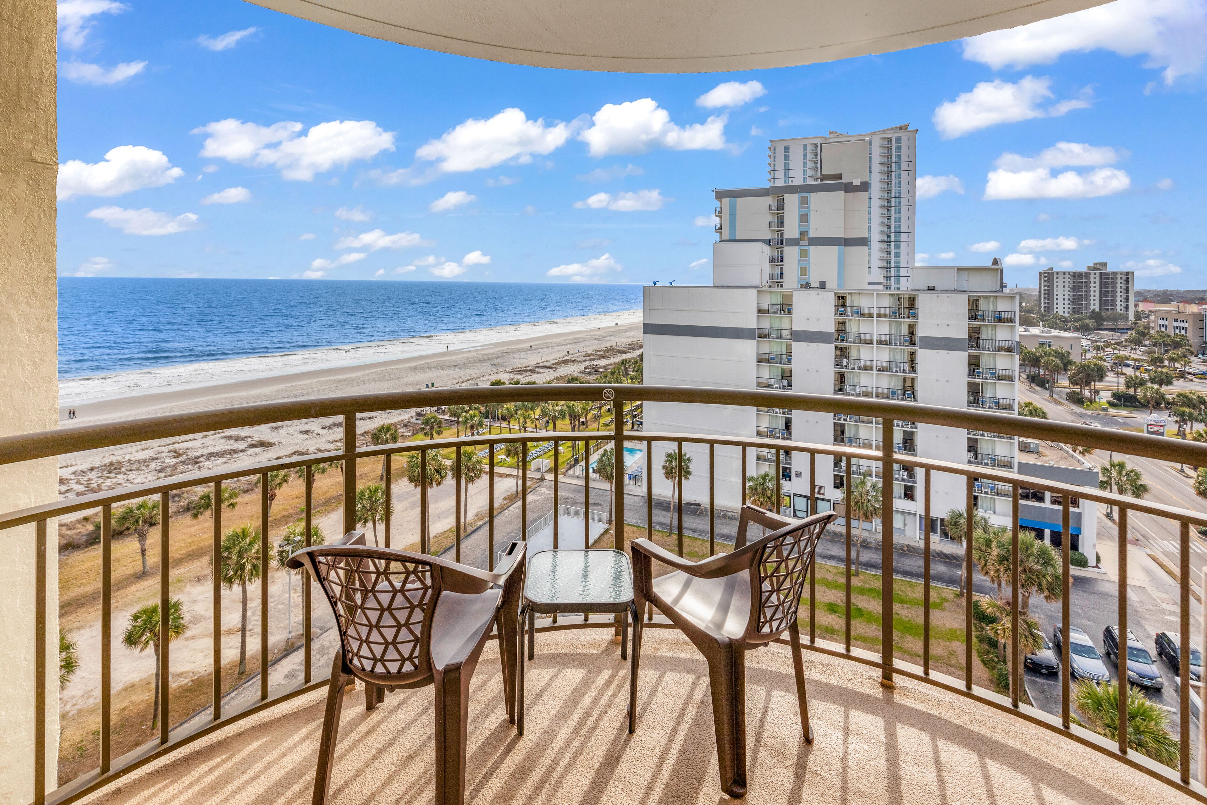 Ein Balkon mit Blick auf Strand und Meer, ausgestattet mit zwei Stühlen und einem kleinen Tisch.