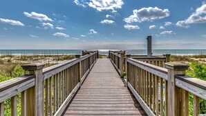 Ein hölzerner Steg führt zu einem Strand, bewölkter Himmel ohne Wolken.