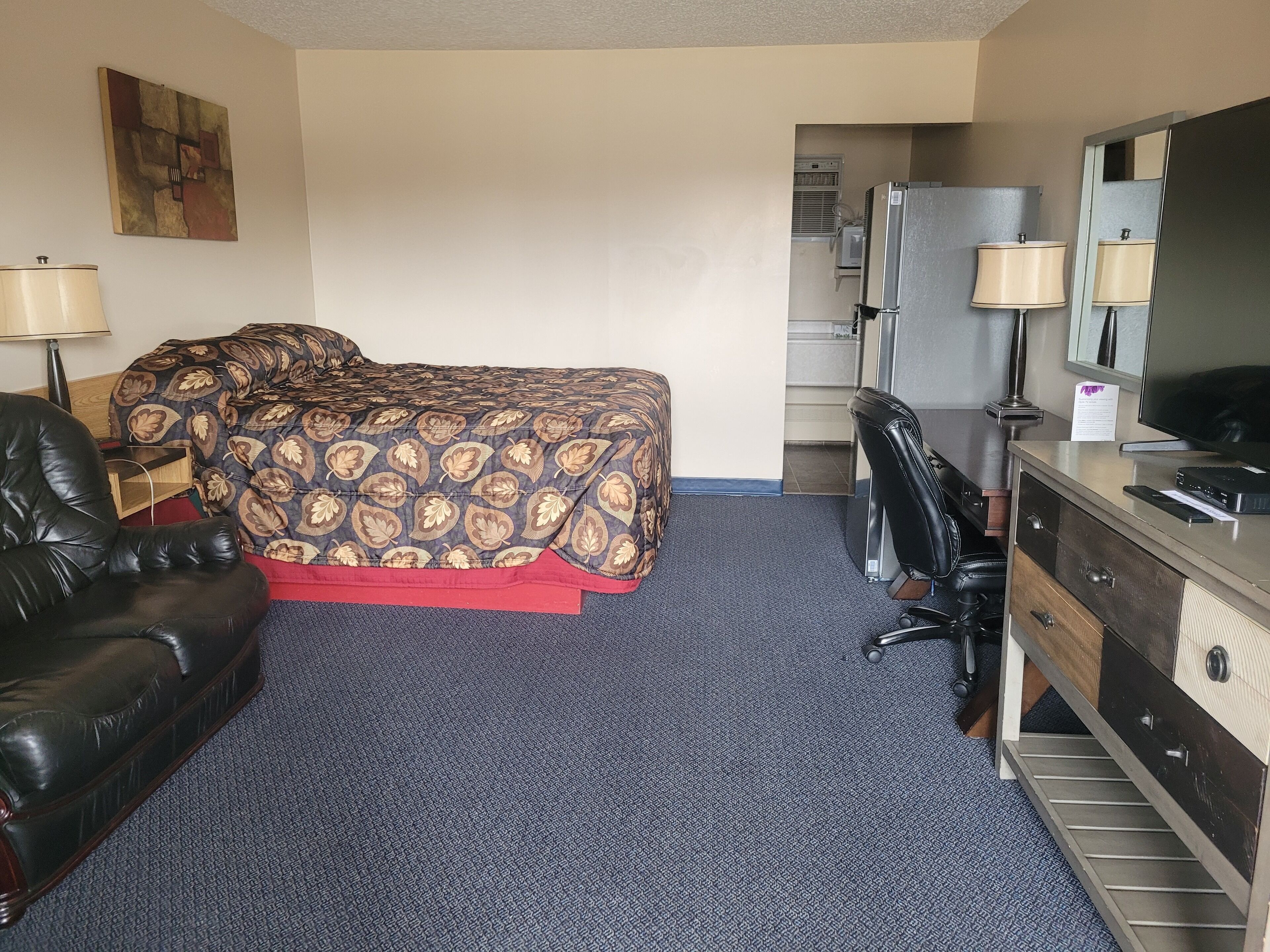 A hotel room with a bed, a desk, a chair, a dresser, and a television.