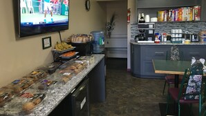 A kitchen area with a TV displaying a sports event, a water dispenser, and a variety of food items on the counter. - Dockside Inn (Cold Lake)