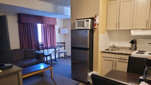 A compact living space with a sofa, dining table, chairs, a refrigerator, microwave, and a small kitchen area with a sink and stove. - Dockside Inn (Cold Lake)