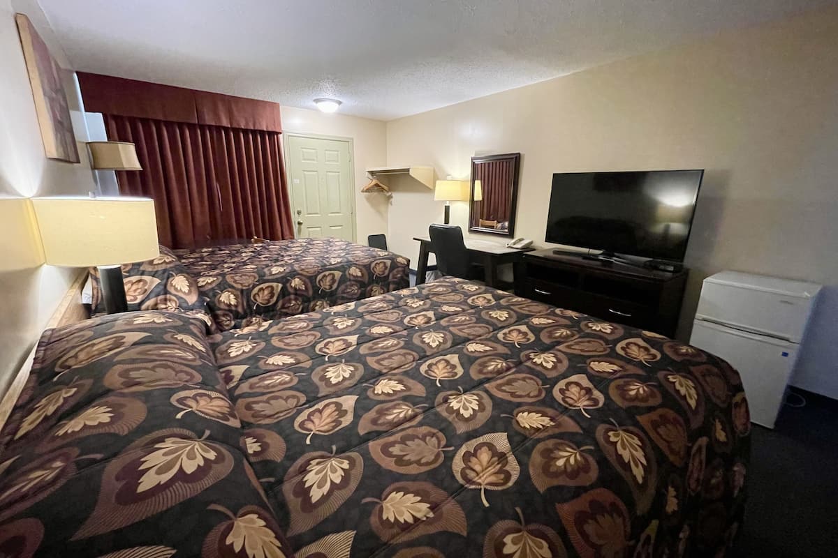 A hotel room with two beds, a television, a desk, a chair, and a small refrigerator.