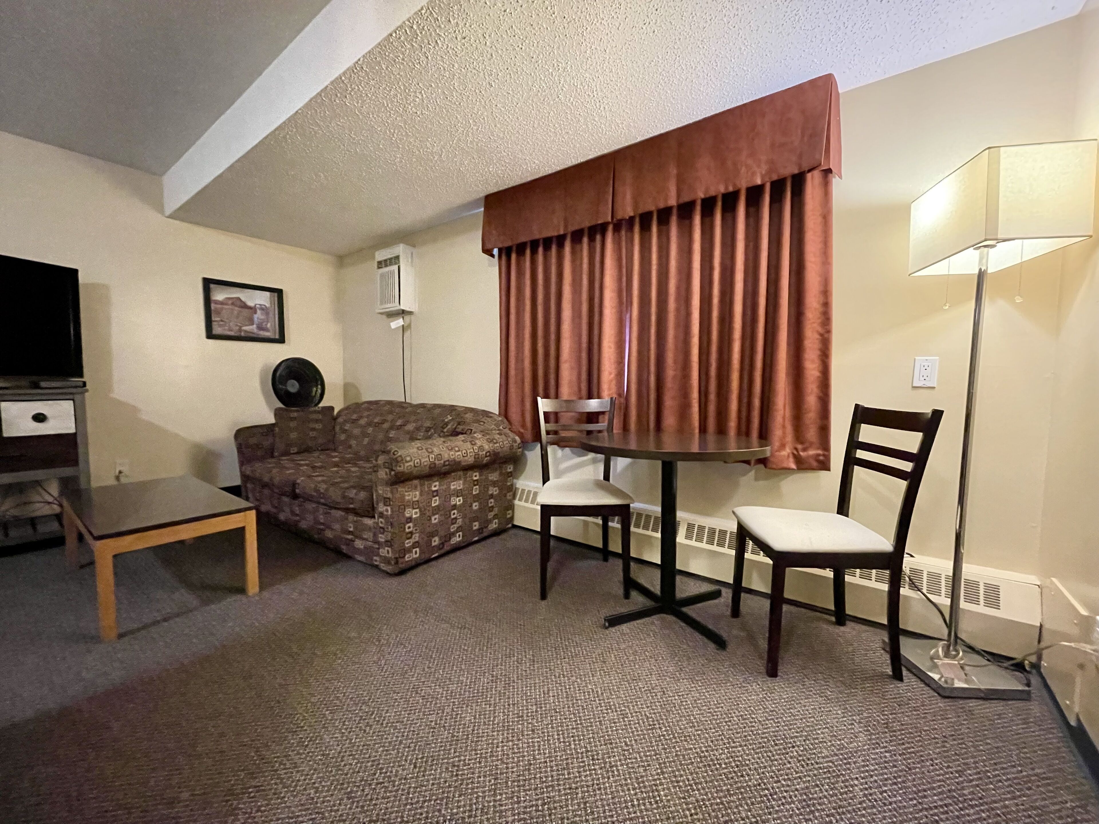 Une chambre d’hôtel de taille réduite, comprenant un canapé, une petite table, une chaise, une lampe et un téléviseur.