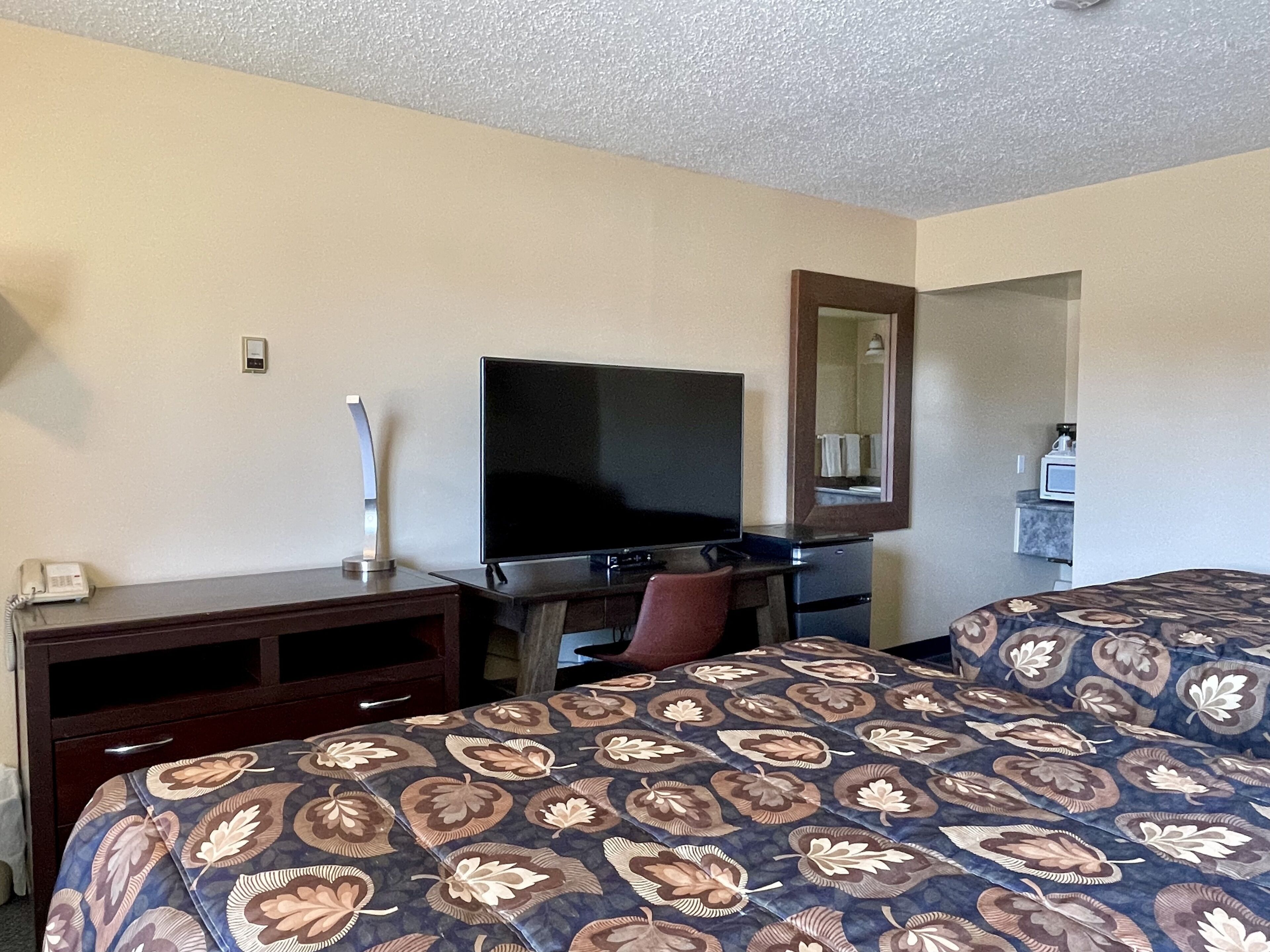 A hotel room with a bed, a desk with a flat-screen TV, a telephone, and a mirror.