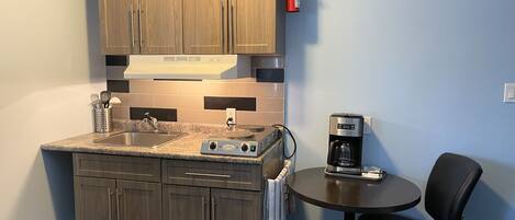 A compact kitchen with wooden cabinets, a built-in stove, a coffee maker, and a small table with a chair.