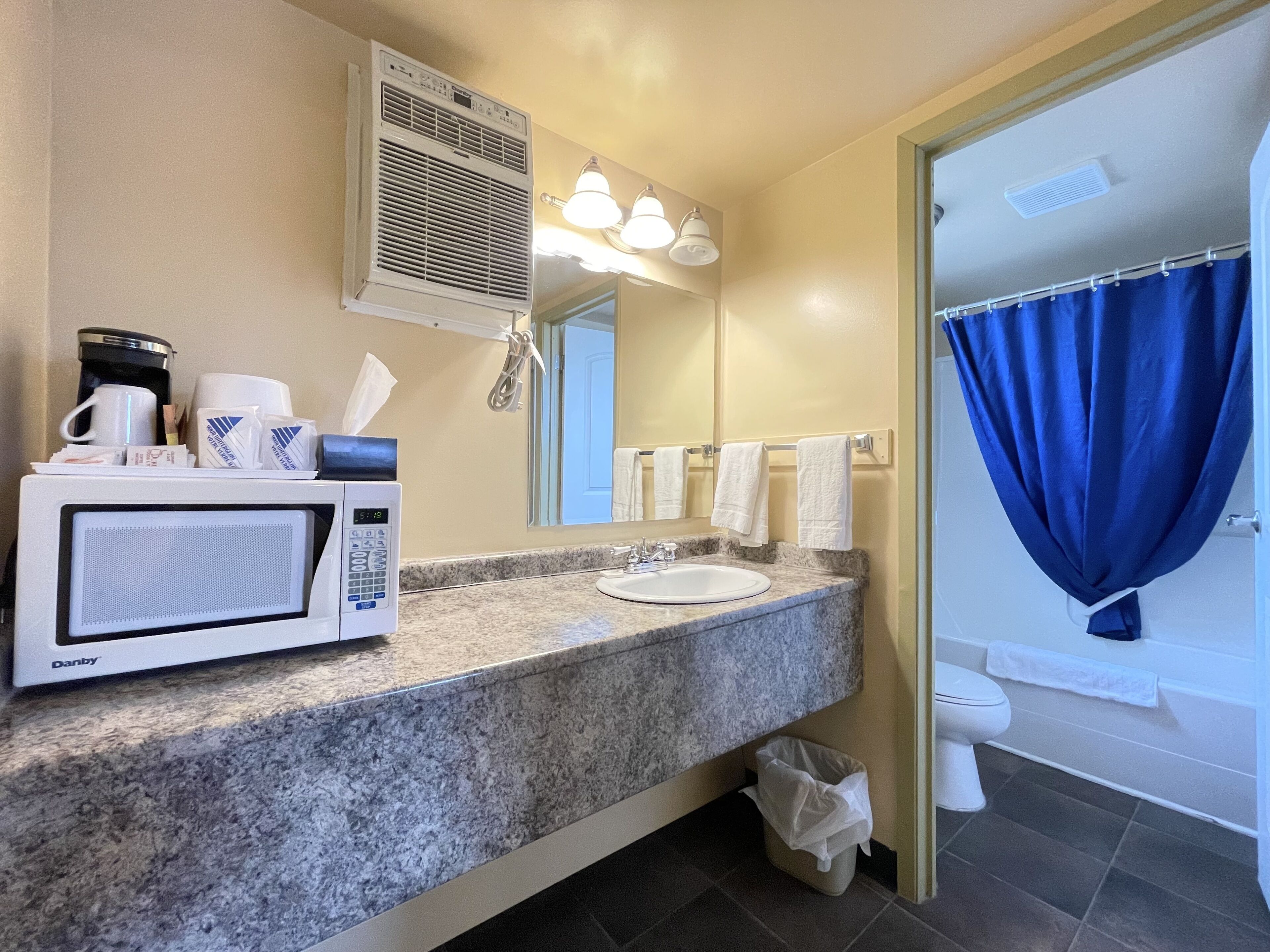 A bathroom with a sink, mirror, towel rack, shower curtain, and a microwave on the counter.