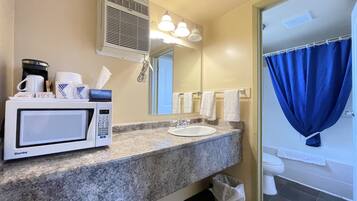 A bathroom with a sink, mirror, towel rack, shower curtain, and a microwave on the counter.