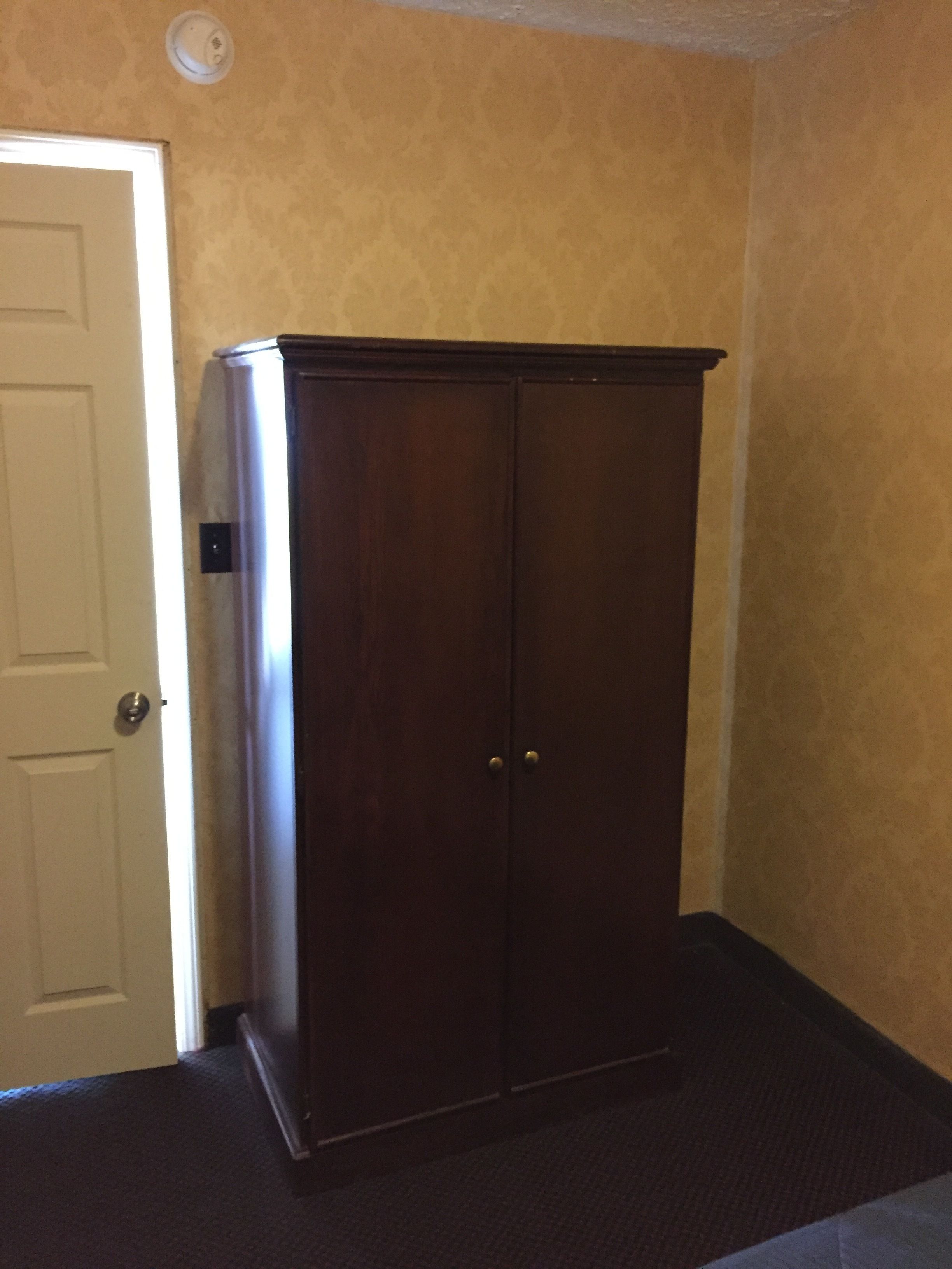 A room with a dark wooden wardrobe, a white door, and patterned wallpaper.