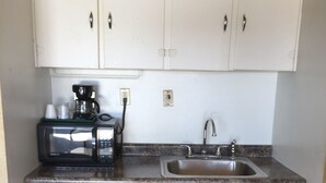 Cocina compacta con armarios de madera, un lavamanos de acero inoxidable, una cafetera y un microondas.