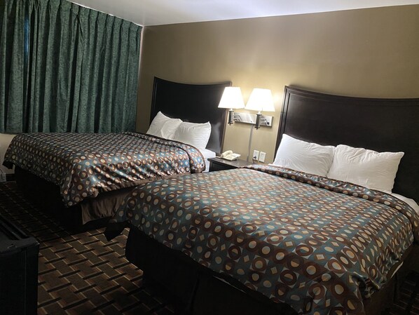 A hotel room with two beds, a nightstand, a lamp, and a telephone.
